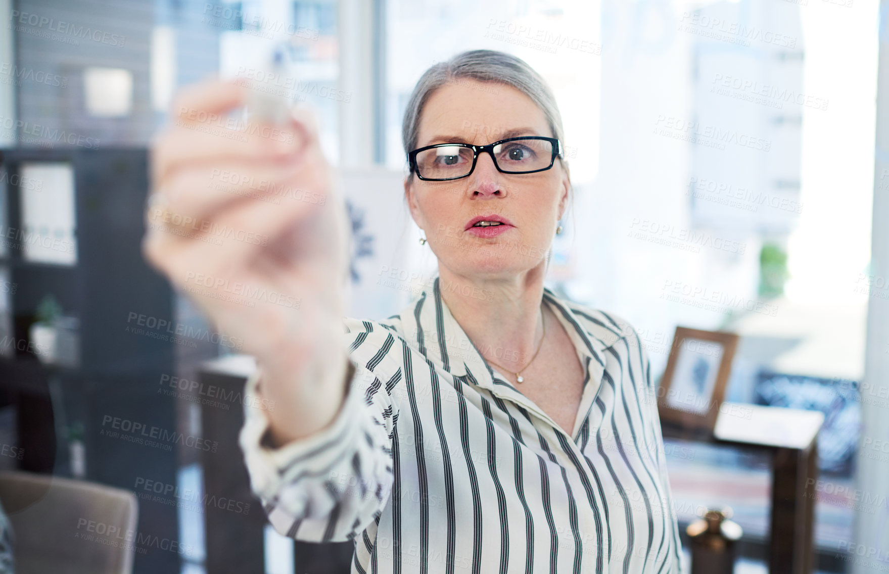 Buy stock photo Shot of a mature businesswoman writing notes on a glass wall in an office