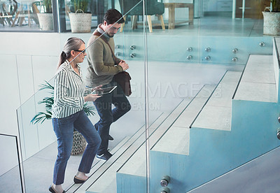 Buy stock photo Shot of two businesspeople using a digital tablet together while walking up a staircase in an office