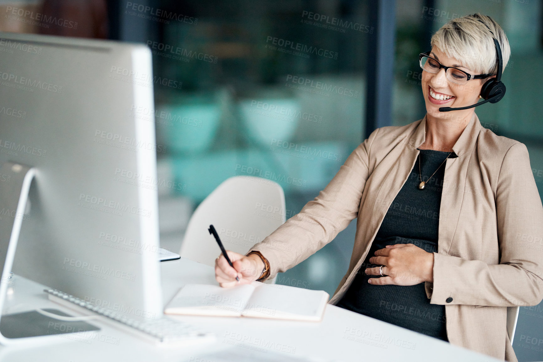 Buy stock photo Shot of a pregnant businesswoman wearing a headset while writing notes in an office