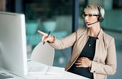 Buy stock photo Shot of a pregnant businesswoman wearing a headset while working on a computer in an office