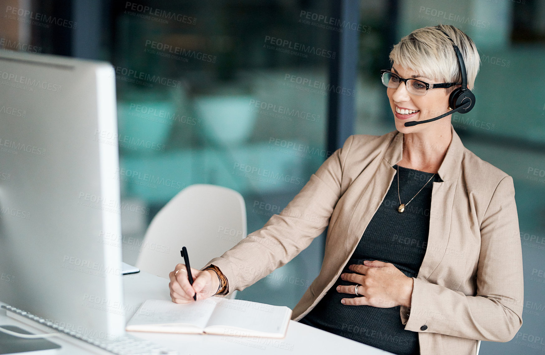 Buy stock photo Shot of a pregnant businesswoman wearing a headset while writing notes in an office