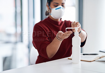 Buy stock photo Shot of a young businesswoman using hand sanitiser in an office