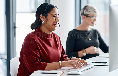 Buy stock photo Shot of a young businesswoman wearing a headset while working on a computer alongside a colleague in an office