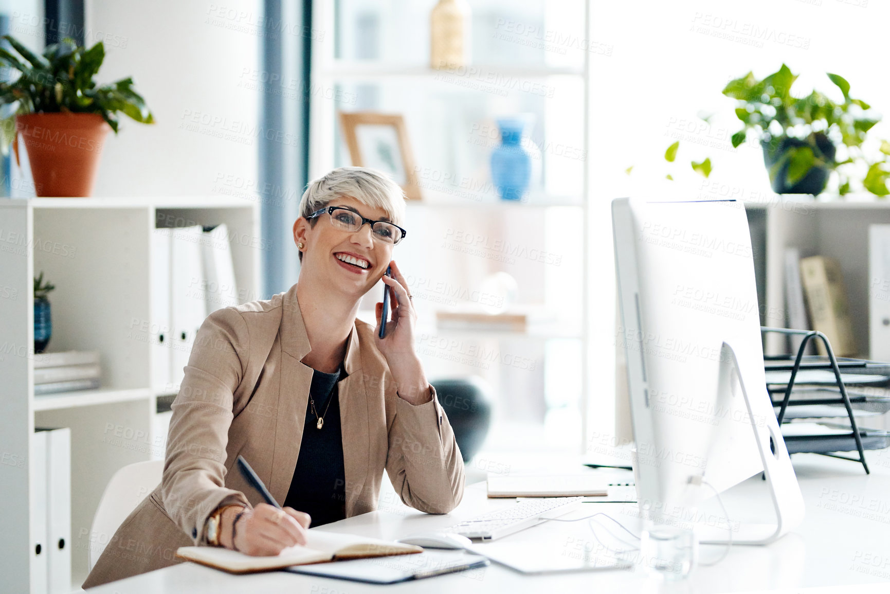 Buy stock photo Shot of a young businesswoman writing notes while talking on a cellphone in an office