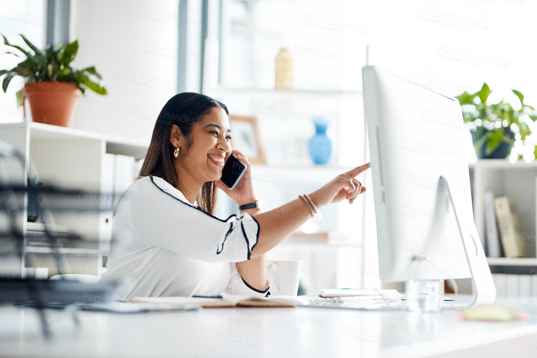 Buy stock photo Shot of a young businesswoman talking on a cellphone while working on a computer in an office