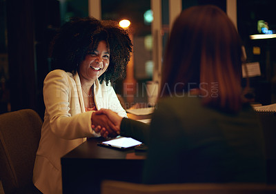 Buy stock photo Shot of two businesswomen shaking hands in an office at night