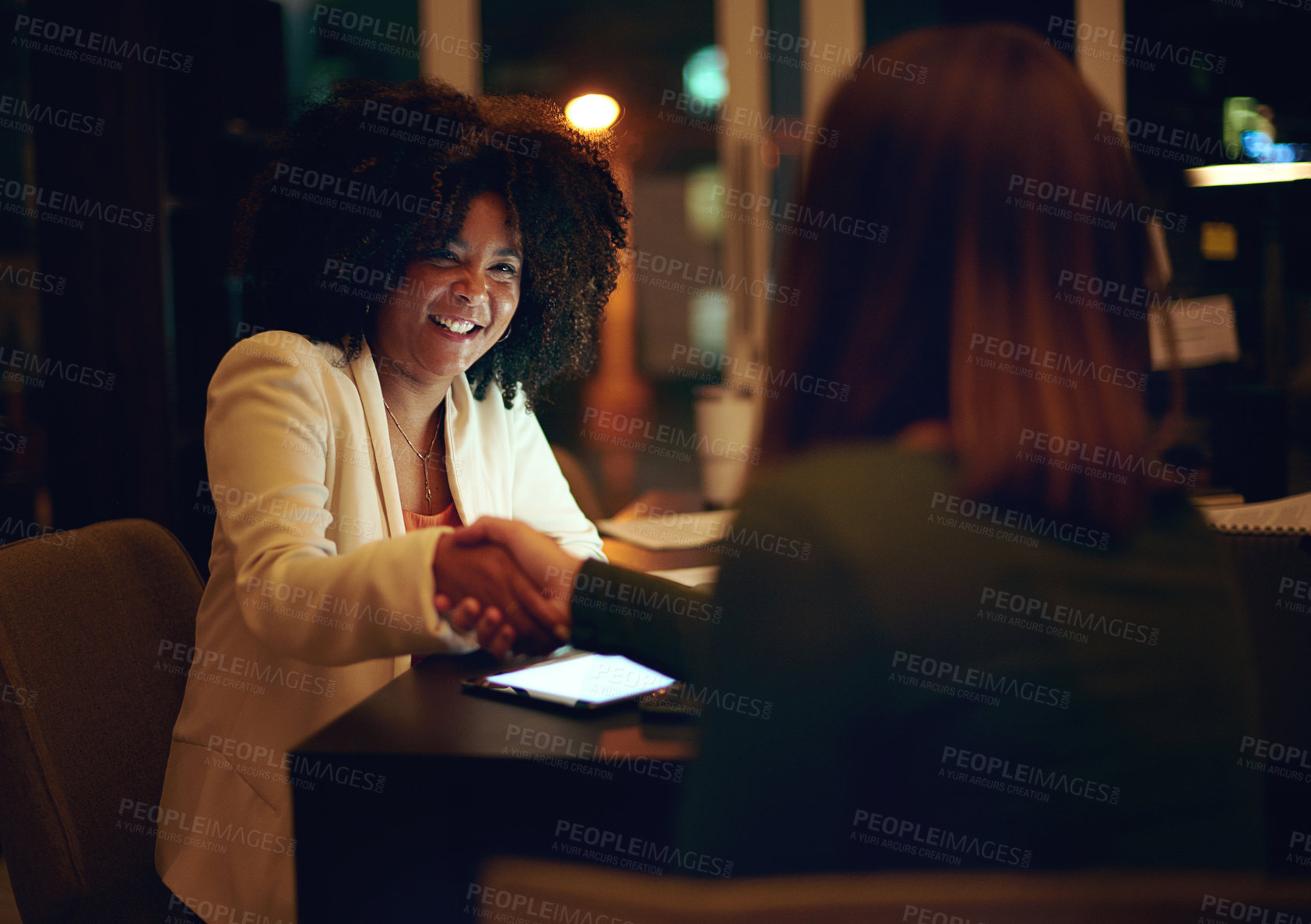 Buy stock photo Shot of two businesswomen shaking hands in an office at night