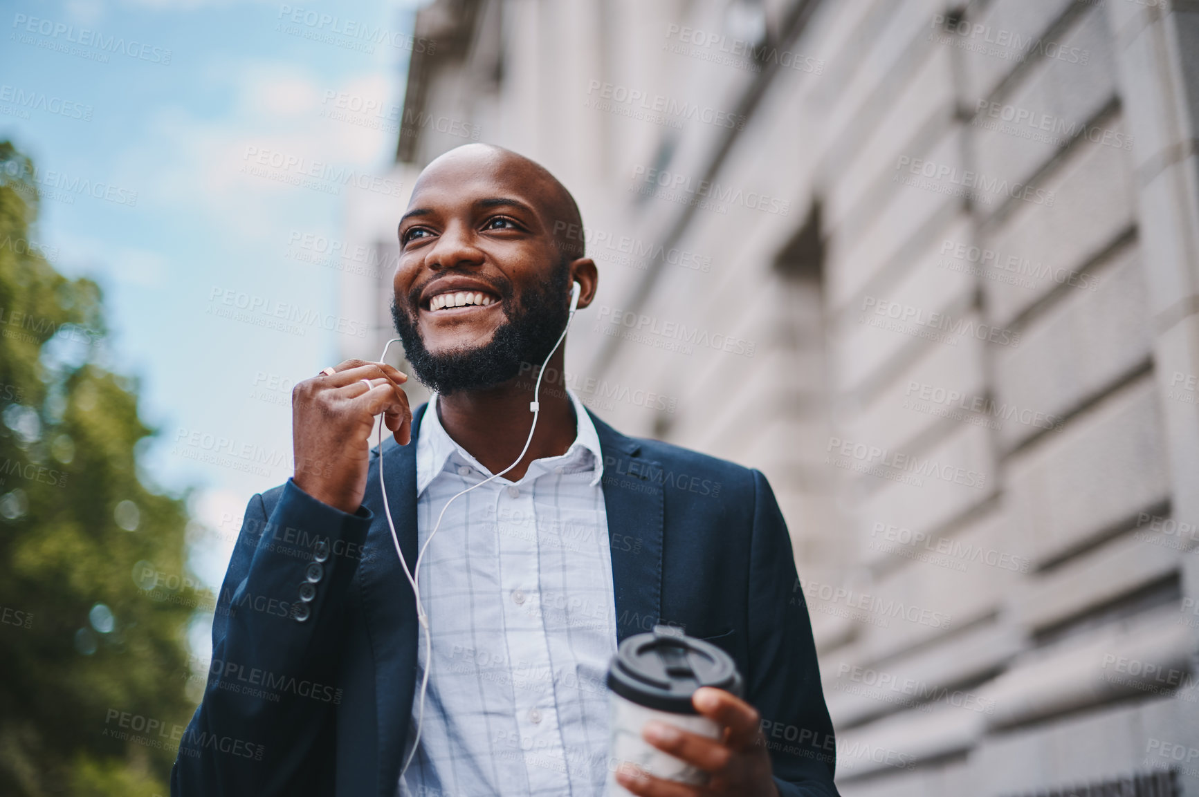 Buy stock photo Shot of a businessman holding a coffee and listening to music through earphones while walking through the city