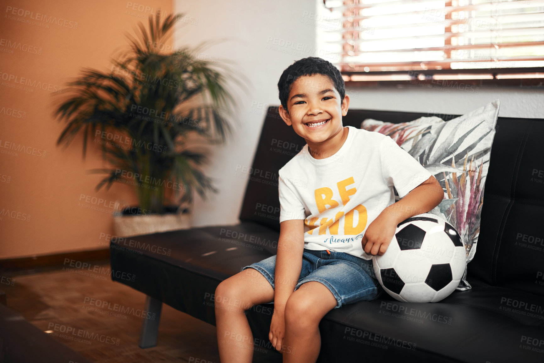 Buy stock photo Portrait, happy and child relax with ball on sofa for football game, fun activity and motor growth of childhood . Smile, boy and rest on couch for practice, sport and development at house living room