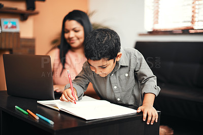 Buy stock photo Shot of an adorable little boy colouring in at home with his mother using a laptop in the background