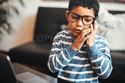 Buy stock photo Shot of an adorable little boy talking on a cellphone while using a laptop at home