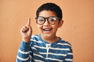 Buy stock photo Child, glasses and portrait with hand raised in studio for knowledge, answer and solution to question. Happy, boy student and smart with specs for info, growth or problem solving on orange background