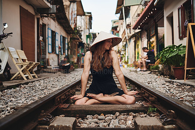 Buy stock photo Shot of a woman wearing a conical hat while sitting on a railway track