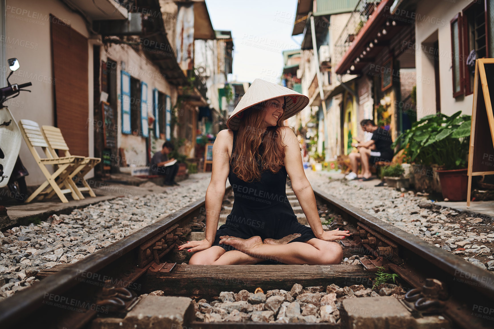 Buy stock photo Shot of a woman wearing a conical hat while sitting on a railway track