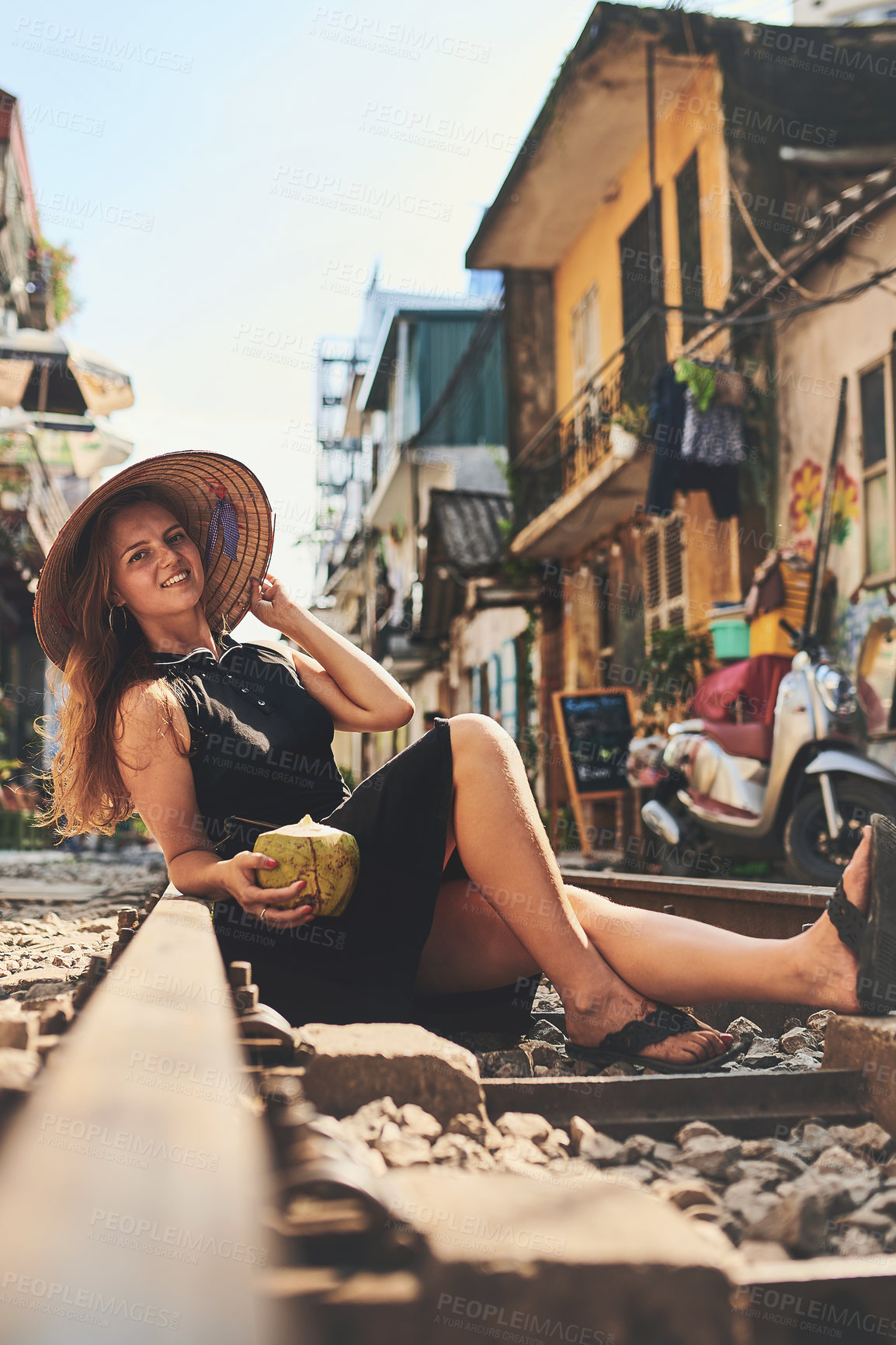 Buy stock photo Shot of a woman having coconut water while relaxing on the train tracks in the streets of Vietnam