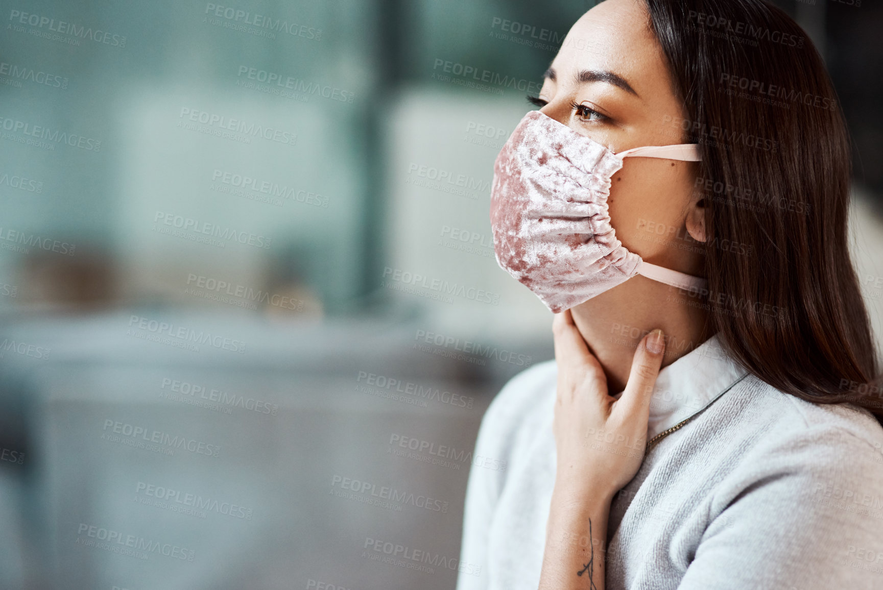 Buy stock photo Shot of a young businesswoman wearing a mask and rubbing her throat in an office