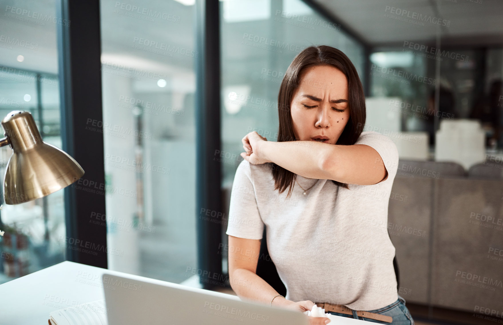 Buy stock photo Shot of a young businesswoman coughing into her elbow in an office