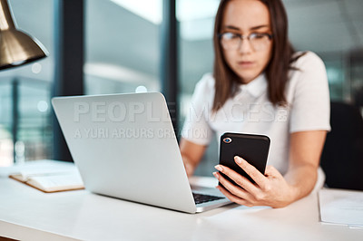 Buy stock photo Shot of a young businesswoman using a cellphone and laptop in an office