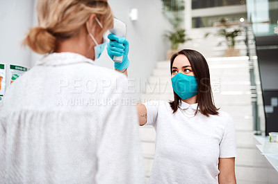 Buy stock photo Shot of a young woman using an infrared thermometer to take the temperature of a colleague in an office