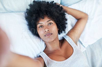 Buy stock photo Cropped shot of a young woman taking a selfie while lying in bed