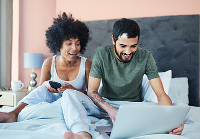 Buy stock photo Shot of a couple looking at something on a laptop while sitting on their bed