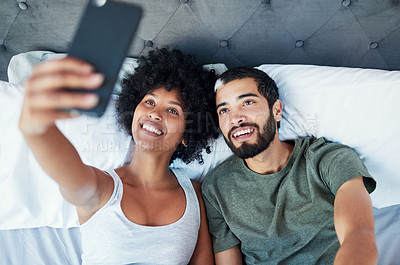 Buy stock photo Shot of a young couple taking a selfie while lying in bed