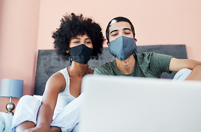 Buy stock photo Shot of a young couple wearing masks while using a laptop at home