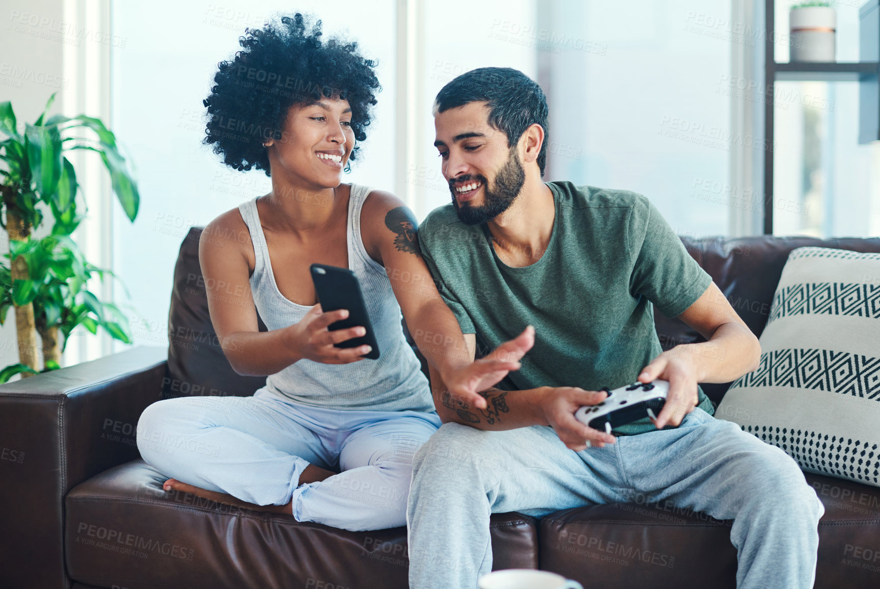 Buy stock photo Shot of a woman showing her boyfriend something on her cellphone while he plays video games