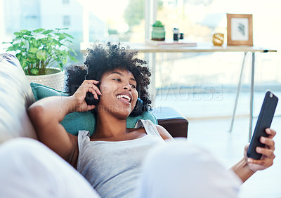 Buy stock photo Shot of a woman using her cellphone while listening to music through headphones at home