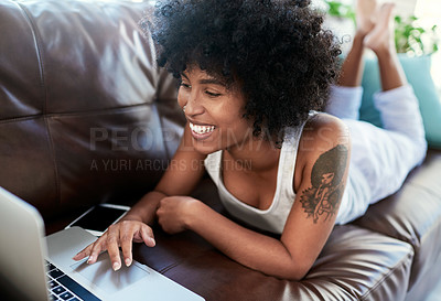 Buy stock photo Shot of a young woman using her laptop while relaxing on the sofa at home