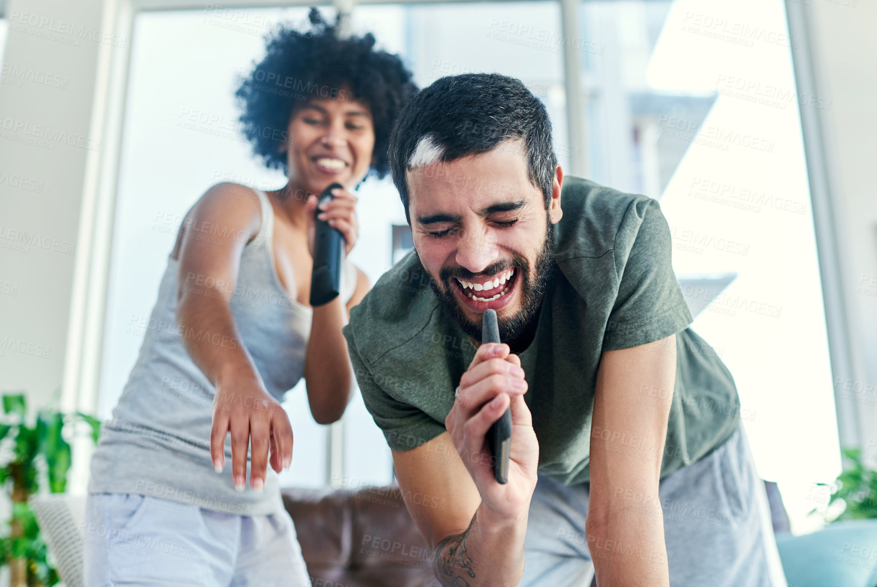 Buy stock photo Couple, music or humor with singing in home for karaoke, radio or bonding fun with remote control. People, love or interracial relationship in lounge with playlist, songs or album for jokes on break