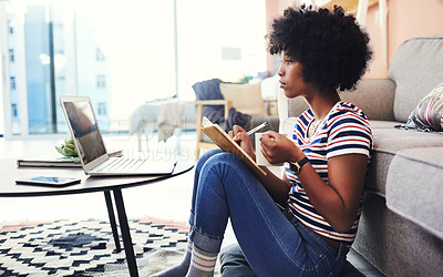 Buy stock photo Shot of a young woman making notes while using her laptop