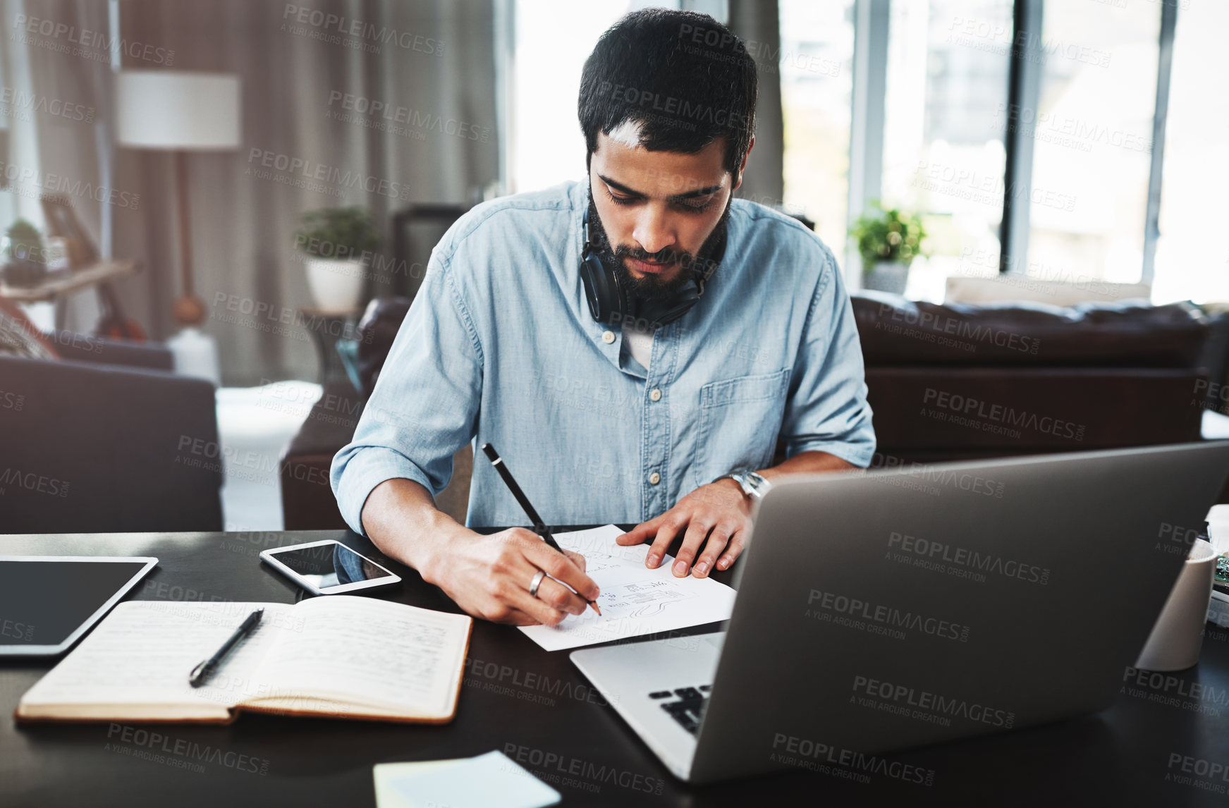 Buy stock photo Shot of a young man making notes while busy working from home