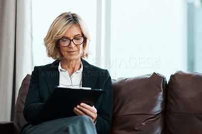 Buy stock photo Shot of a mature psychologist sitting on a sofa and writing notes on a clipboard