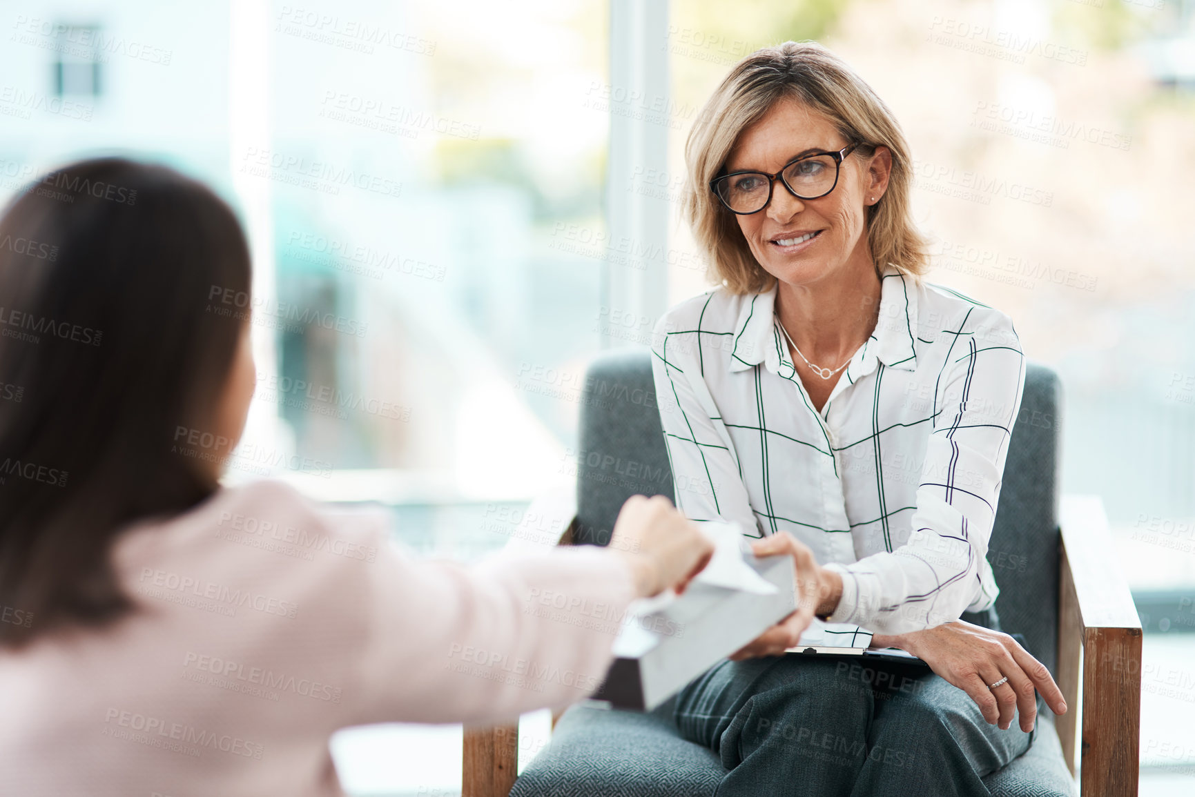 Buy stock photo Shot of a mature psychologist offering her patient tissues during a therapeutic session