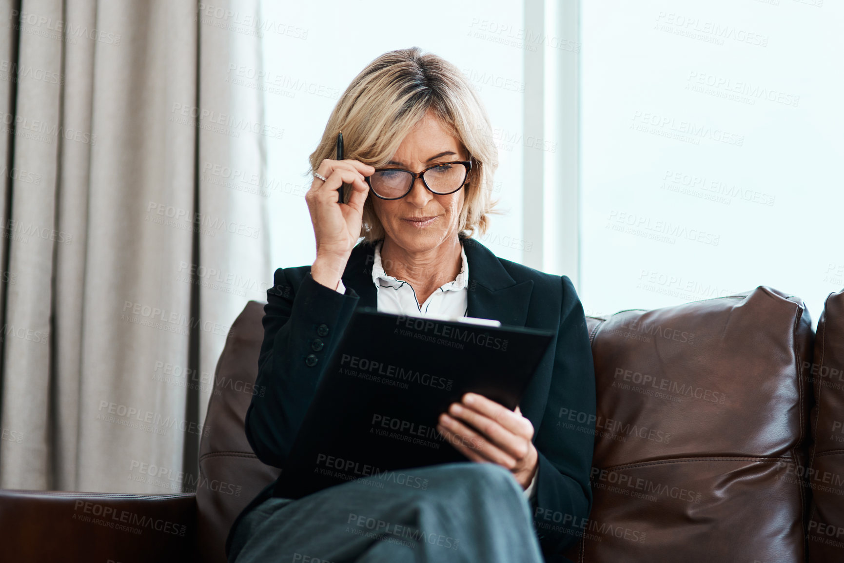 Buy stock photo Shot of a mature psychologist sitting on a sofa and writing notes on a clipboard