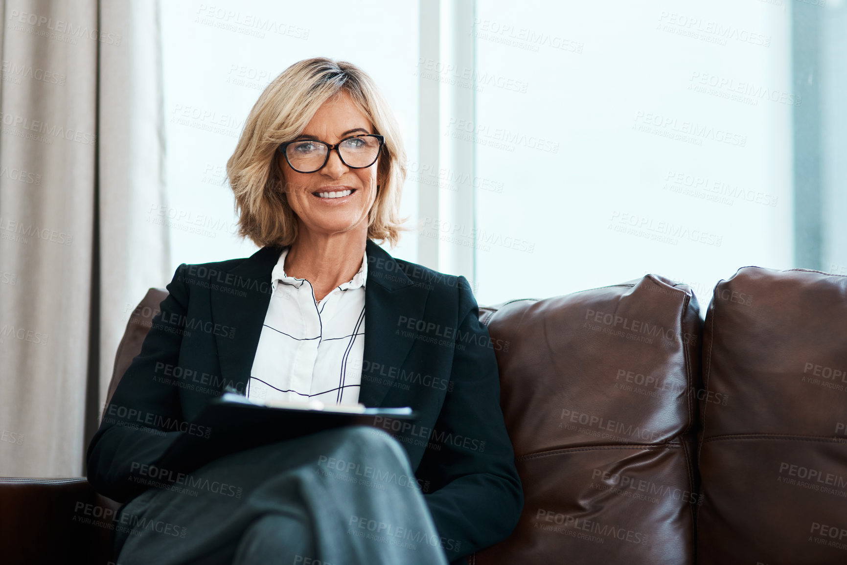 Buy stock photo Shot of a mature psychologist sitting on a sofa and writing notes on a clipboard