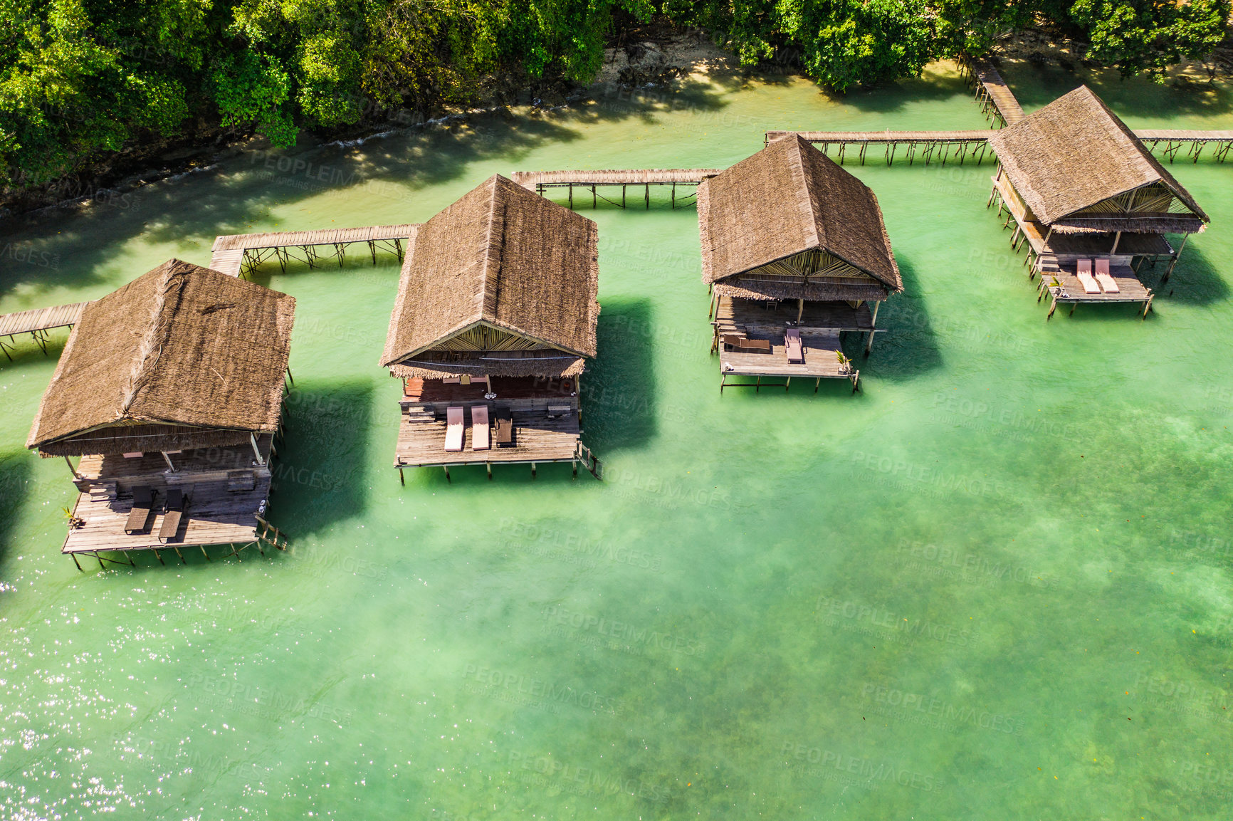 Buy stock photo Aerial, buildings and resort by tropical ocean with bridge, island and trees on beach for tourism agency. Jetty, hotel and hospitality by sea, adventure and drone in nature with water in Raja Ampat