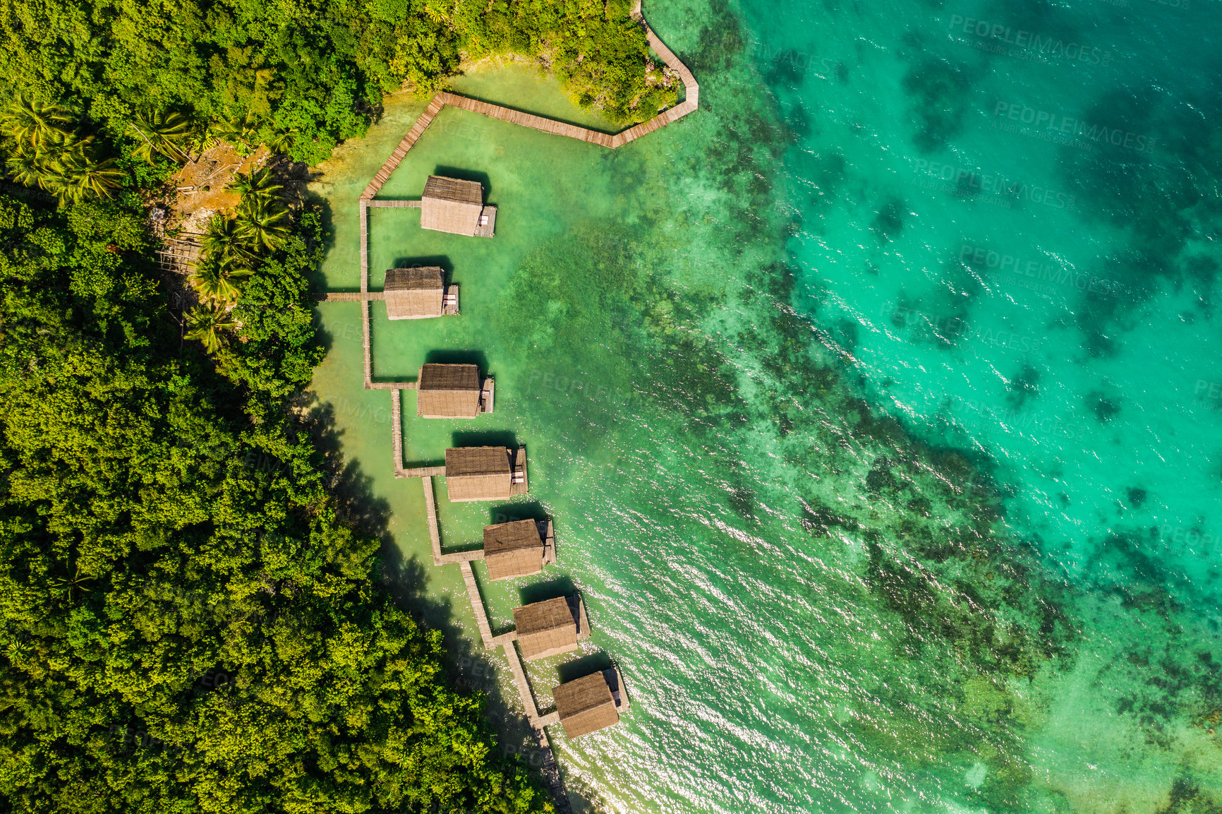 Buy stock photo Aerial, buildings and lodge by tropical sea with bridge, island and trees on beach for tourism agency. Jetty, hotel and outdoor with ocean, hospitality and drone in nature with waves in Raja Ampat
