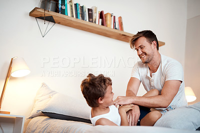Buy stock photo Shot of a man tickling his son while lying in bed