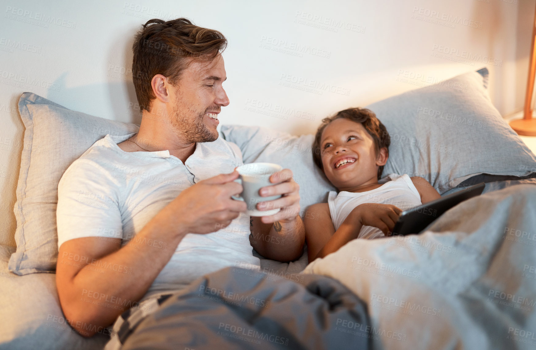 Buy stock photo Shot of a young boy using a digital tablet while lying in bed with his dad