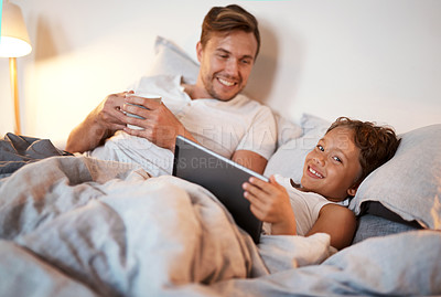Buy stock photo Shot of a young boy using a digital tablet while lying in bed with his dad