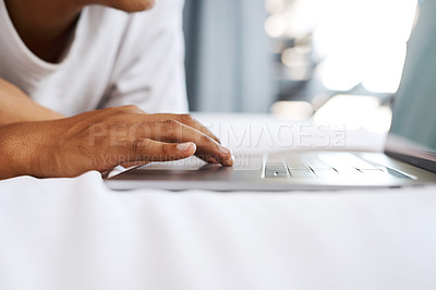Buy stock photo Cropped shot of an unrecognizable man using his laptop while lying on his bed