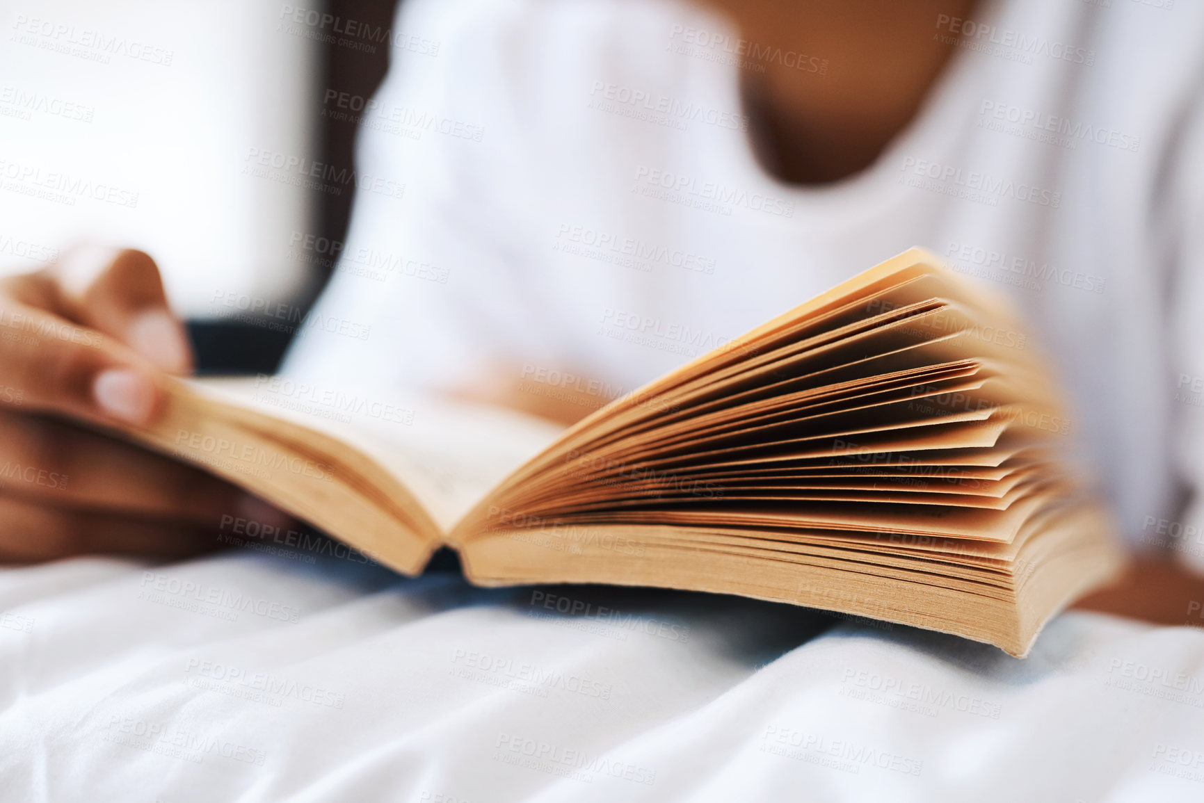 Buy stock photo Cropped shot of a young man reading a book while lying on his bed