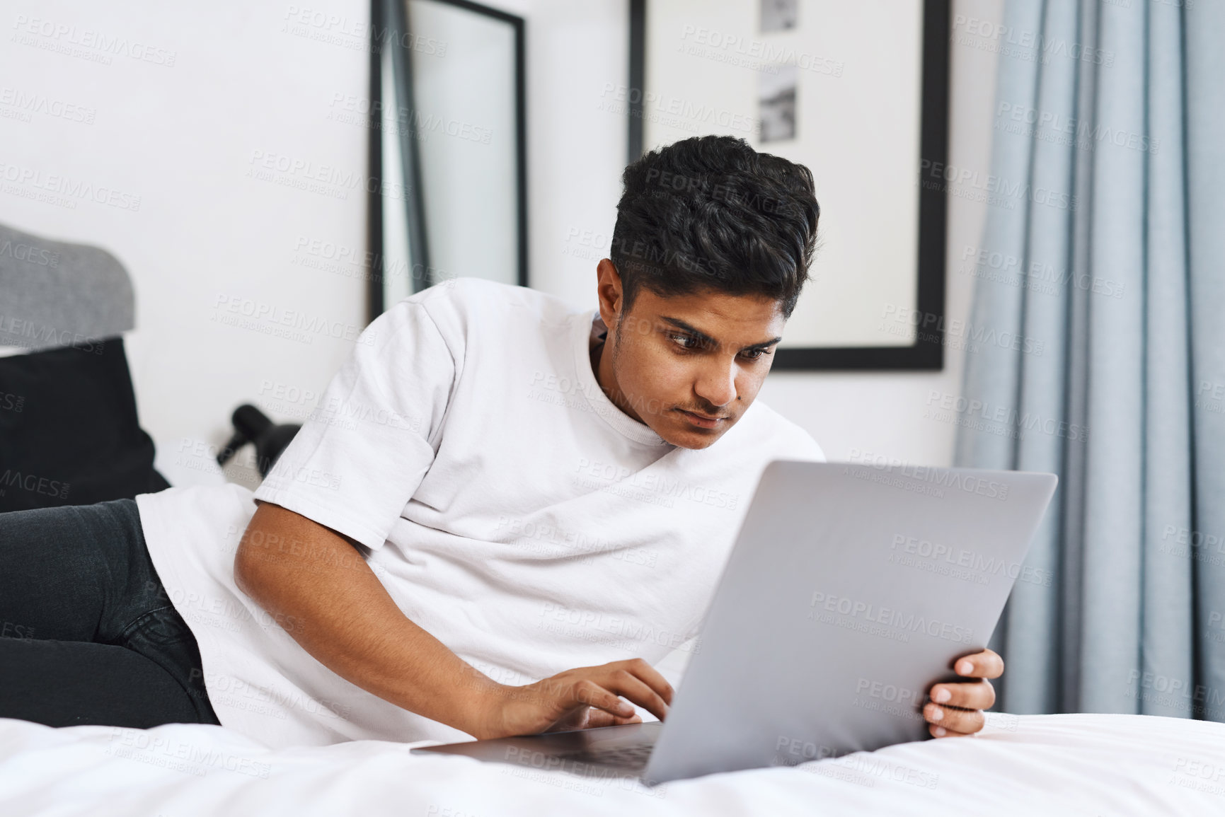 Buy stock photo Cropped shot of an young man using his laptop while lying on his bed