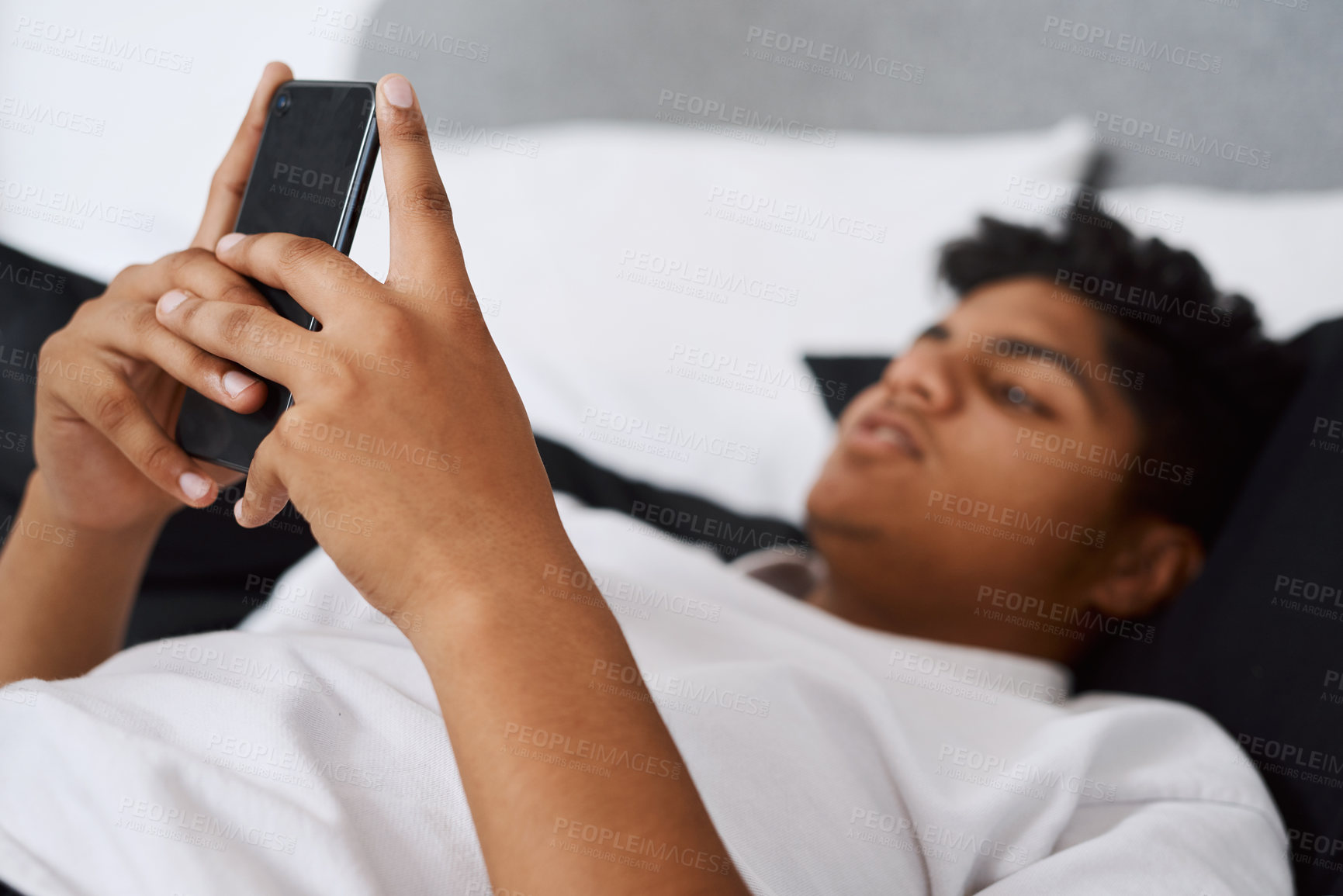 Buy stock photo Shot of a young man using his cellphone while lying on his bed