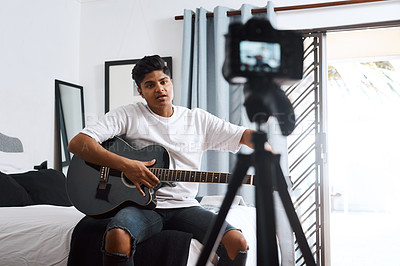 Buy stock photo Shot of a young man recording himself at home while playing the guitar