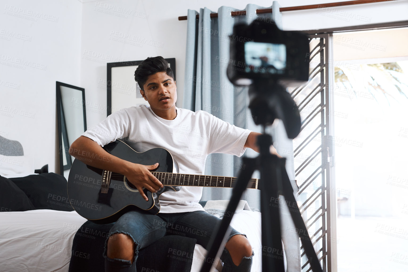 Buy stock photo Shot of a young man recording himself at home while playing the guitar