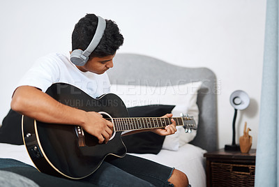 Buy stock photo Shot of a young man wearing headphones while playing the guitar at home
