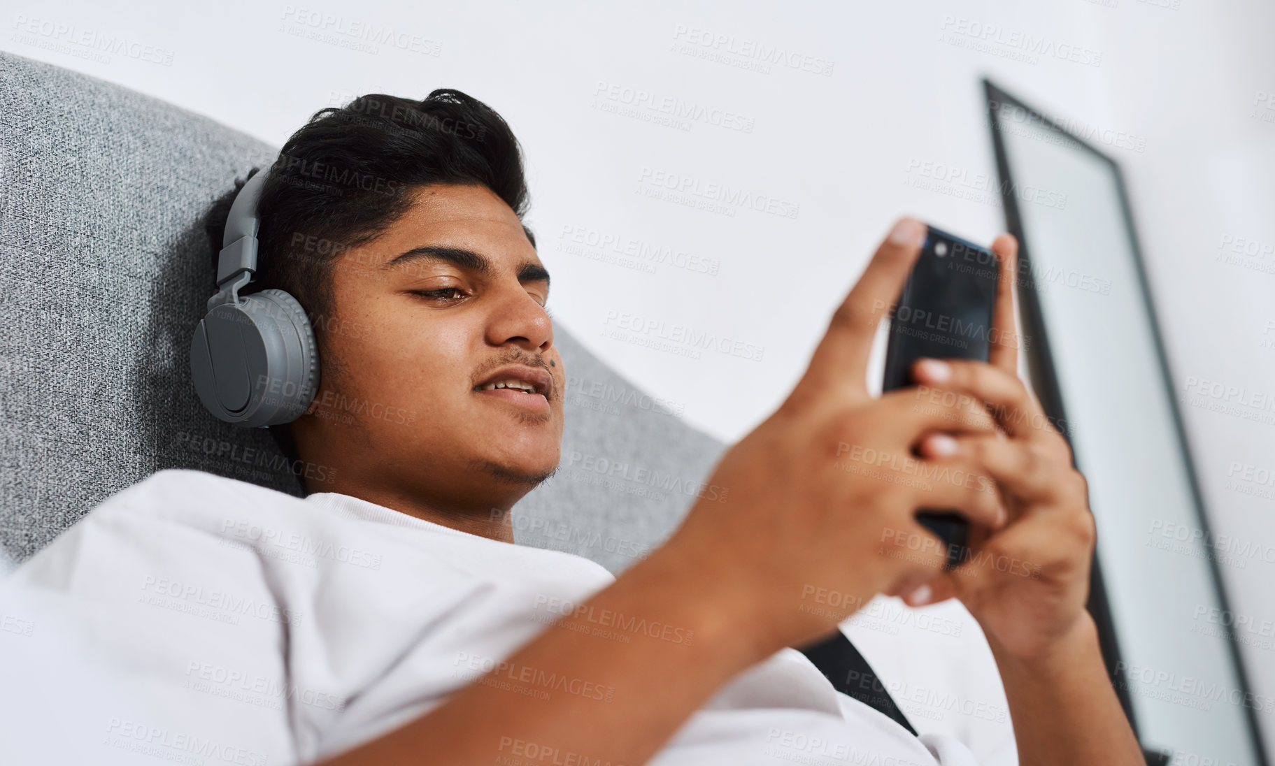 Buy stock photo Teenager, headphones and person with phone in bedroom for internet, connection and listening to song. Happy, boy and smile with technology at home for streaming, audio and update of music playlist